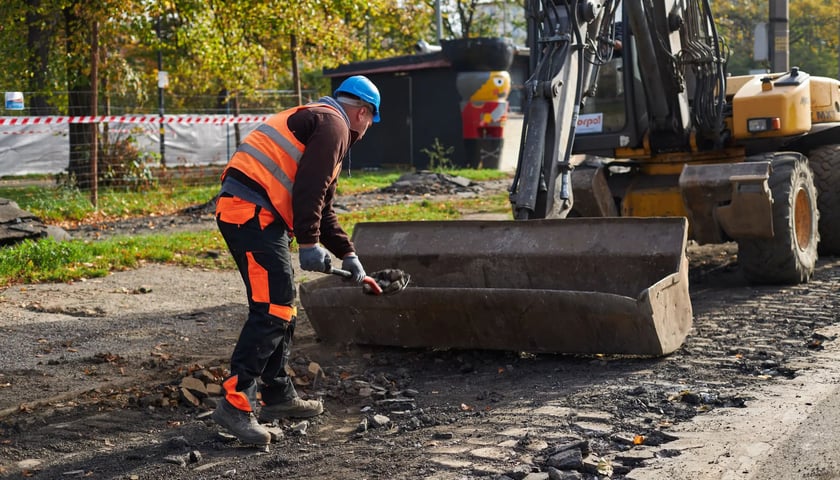 Roboty drogowe, zdjęcie ilustracyjne. Na zdjęciu koparka i pracownik w roboczym kombinezonie