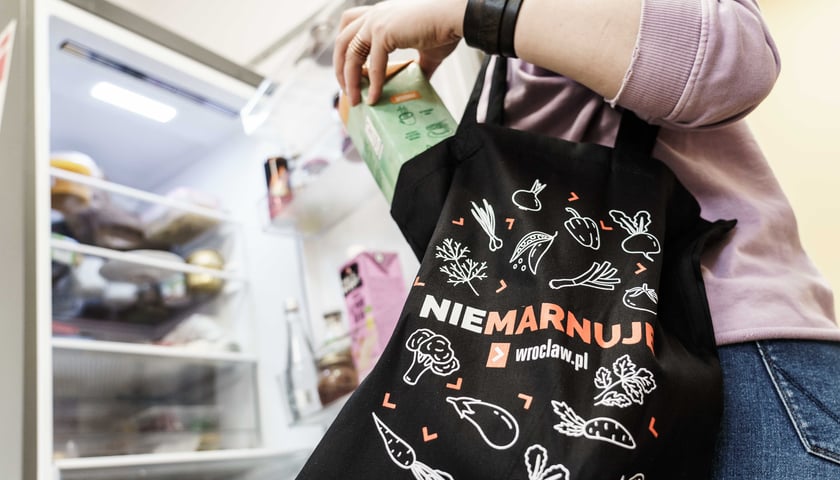 Kobieta wyciąga zakupy z płóciennej torby z napisem ,,Wrocław nie marnuje''