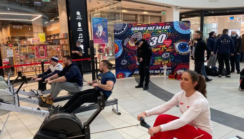 Na zdjęciu kobieta w biało-czerwonym stroju sportowym wiosłuje na ergometrze