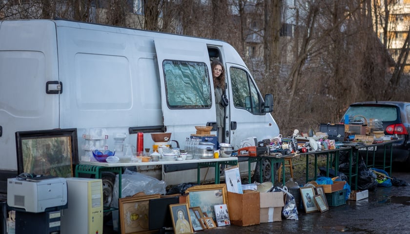 Targowisko na Świebodzkim - 4 lutego 2024. Na zdjęciu widać biały samochód, w drzwiach stoi kobieta. Koło auta są wystawione rzeczy na sprzedaż 