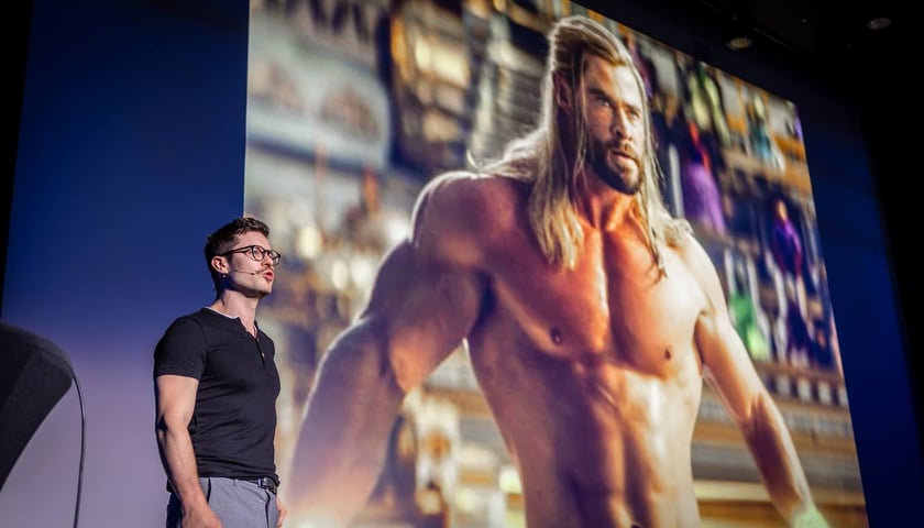 Na zdjęciu Maciej Kaselon opowiada o tym, że czujemy się jak bohaterowie, kiedy możemy poprawić czyjś językowy błąd, na slajdzie za nim filmowy Thor