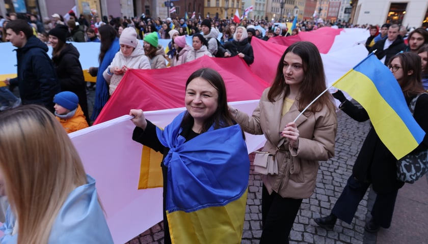 Tłum we wrocławskim Rynku niesie flagę Polski i flagi Ukrainy na znak solidarności z narodem ukraińskim.