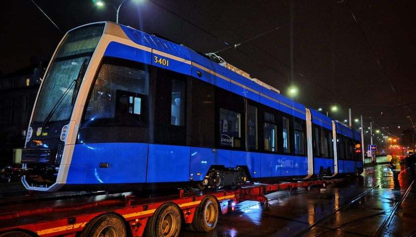 Zdjęcie miasta nocą, przejazd niebieskiego tramwaju na lawecie  