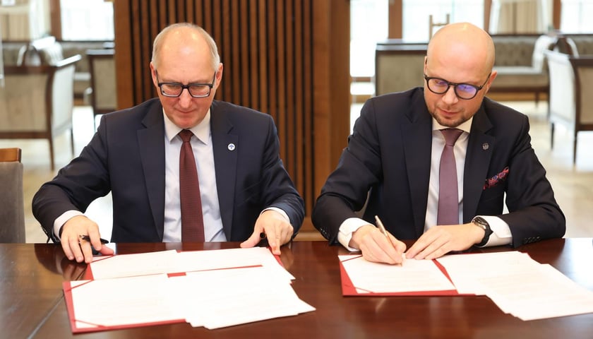Dwóch mężczyzn w garniturach siedzi za stołem, podpisują dokumenty. Od lewej: prof. Arkadiusz Wójs, rektor Politechniki Wrocławskiej i Jakub Mazur, wiceprezydent Wrocławia 