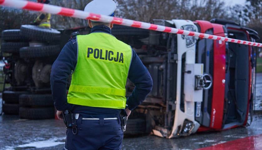 Wypadek drogowy z udziałem ciężarówki, na pierwszym planie policjant. Zdjęcie ilustracyjne