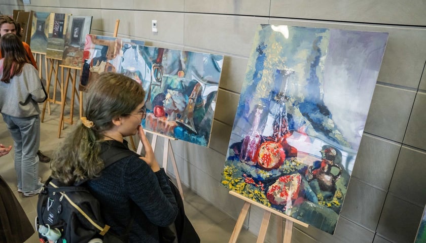 Przed sztalugą stoi młoda dziewczyna i przygląda się obrazowi. Wernisaż wystawy prac uczniów Liceum Sztuk Plastycznych w Bibliotece Uniwersyteckiej (3.04.2024)