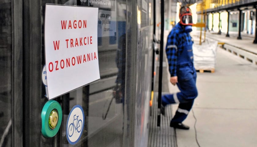 Z wagonu tramwajowego wychodzi w masce pracownik MPK po akcji ozonowania tramwaju na zajezdni Borek