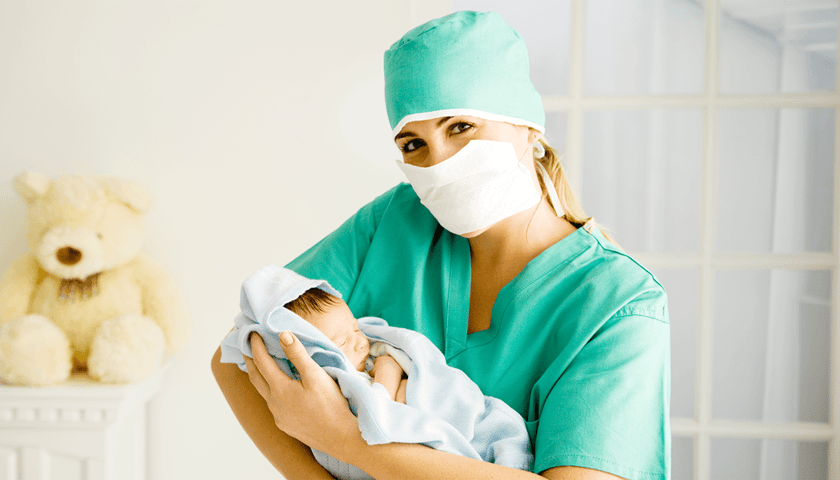 Na zdjęciu: kobieta w medycznym stroju trzyma na rękach noworodka