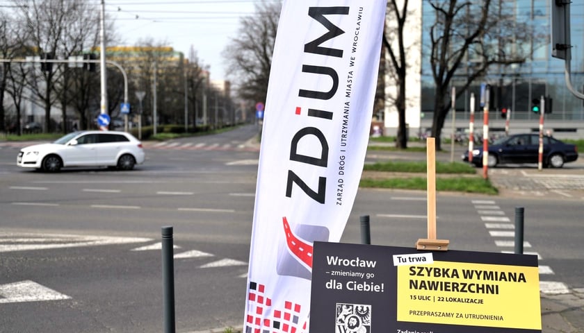 ZDiUM wymienia nawierzchnie 15 ulic. Teraz nadszedł czas na Pilczycką, Sołtysowicką, Karkonoską i Gazową. Na zdjęciu skrzyżowanie, baner ZDiUM oraz tablica z napisem „Tu trwa szybka wymiana nawierzchni”