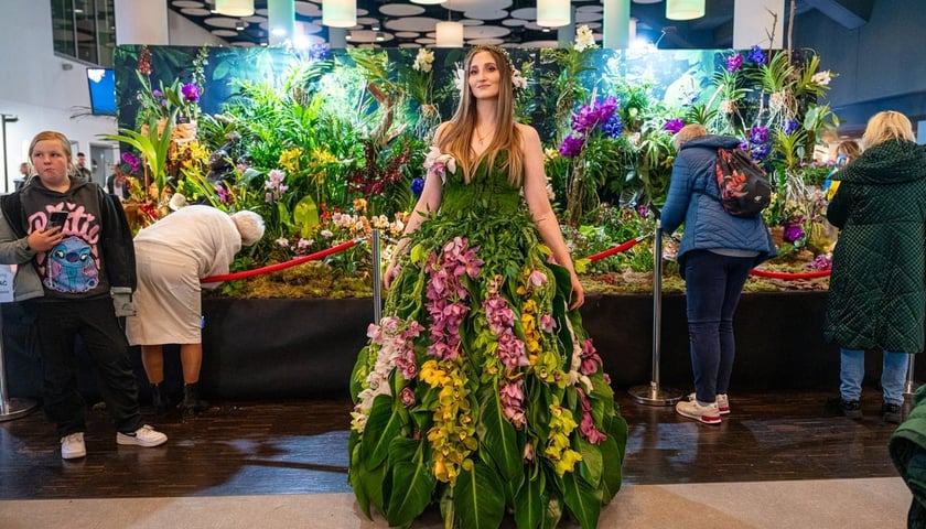 Kobieta w sukni z kwiatów - w tle wystawa na Tarczyński Arenie 