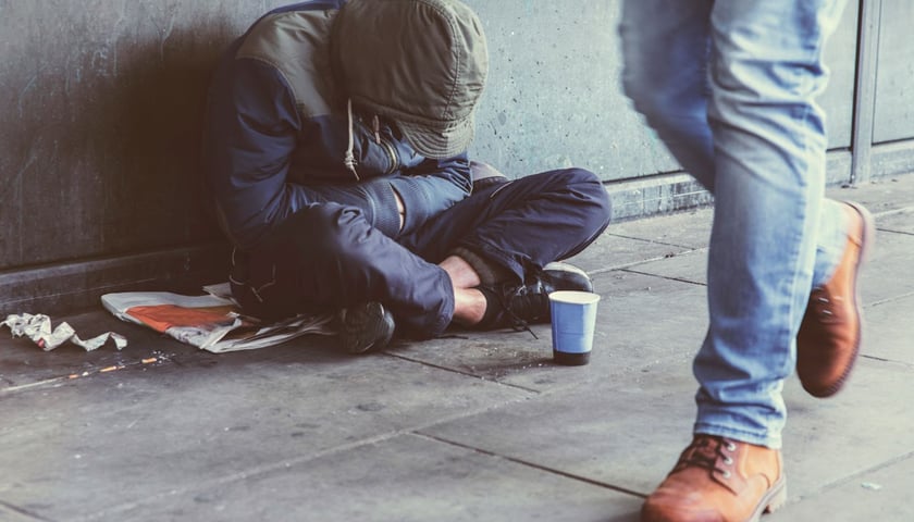 Osoba w kryzysie bezdomności siedząca p oturecku pod ścianą na ulicy
