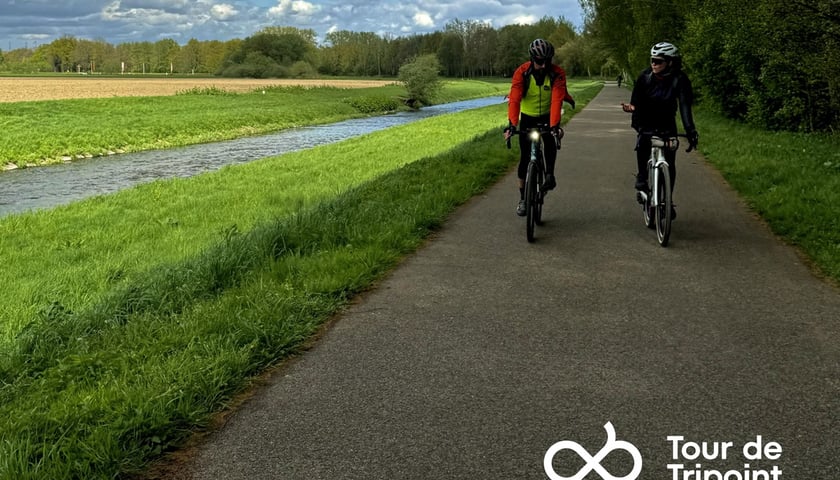 Trasa Tour the Tripoint prowadzi przez malowniczą okolicę. Na zdjęciu dwoje rowerzystów jedzie szosą wzdłuż rzeki