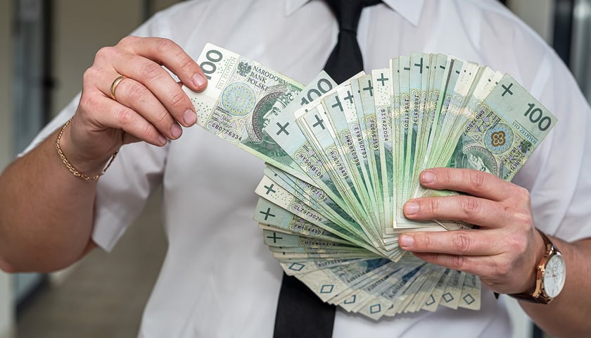 Mężczyzna trzyma w rękach plik banknotów, zdjęcie ilustracyjne