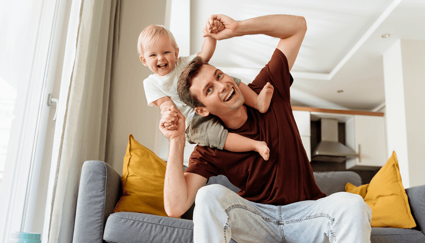 Na zdjęciu młody mężczyzna trzyma rozbawione dziecko na barana