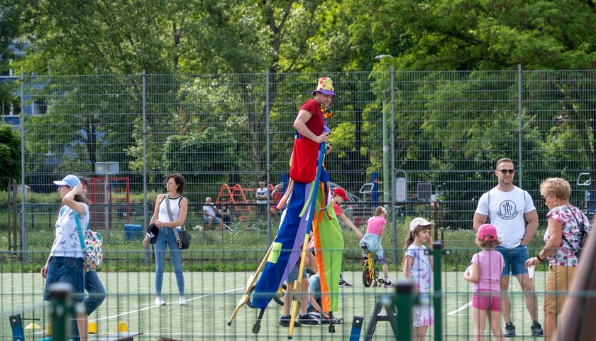 Piknik integracyjny z Kozanowie. W tle szczudlarz i bawiące się dzieci