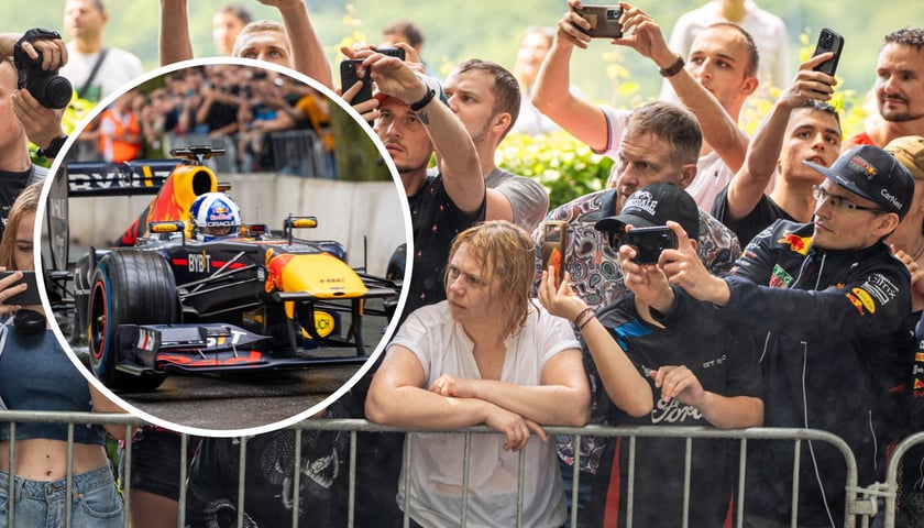 Kobiety, mężczyźni i dzieci patrzą na pojedynek bolidu F1
