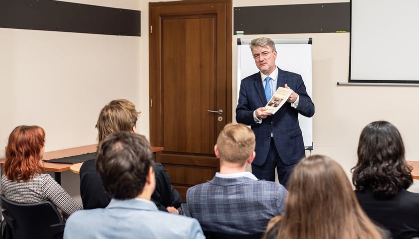 Dr Edward Wąsiewicz, Konsul Honorowy Republiki Austrii we Wrocławiu. Inauguracja Akademii Dyplomatycznej. Na zdjęciu elegancki mężczyzna przemawia przed grupą młodych osób w sali wykładowej