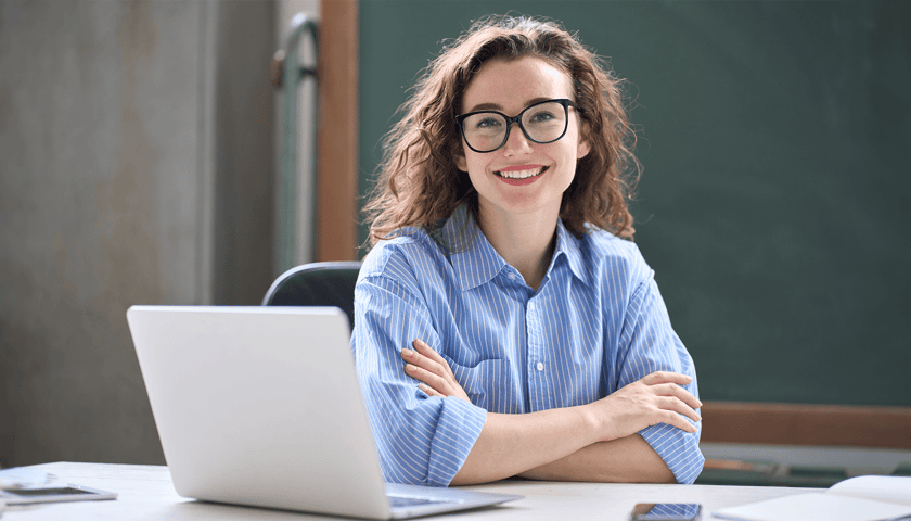 Uśmiechnięta kobieta siedzi przy biurku, przed nią rozłożony laptop (zdjęcie ilustracyjne)