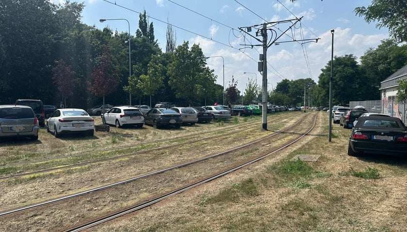 Samochody stojące na trawniku przy torowisku 