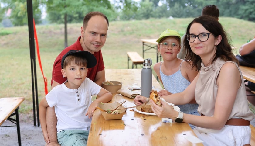 Gastro Miasto 2024 we Wrocławiu. Na zdjęciu mężczyzna, kobieta i dwójka dzieci - uczestnicy festiwalu, siedzą przy stole z jedzeniem 