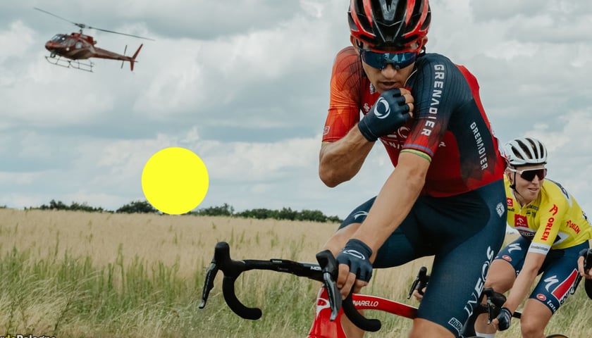 Kolarz na rowerze nawiązujący kontakt przed radio na trasie TdP 2023, widać też żółte kółko i helikopter