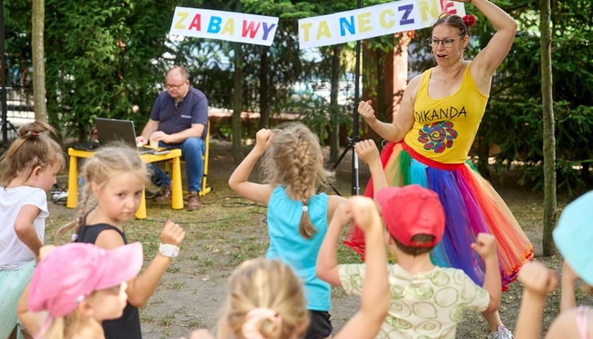 Piknik dla dzieci. Zdjęcie ilustracyjne. Na zdjęciu młoda kobieta tańczy wesoło z dziećmi
