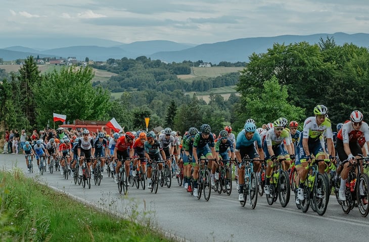 Kolarze wyścigu Tour de Pologne z dwiema polskimi flagami na odcinku górskim