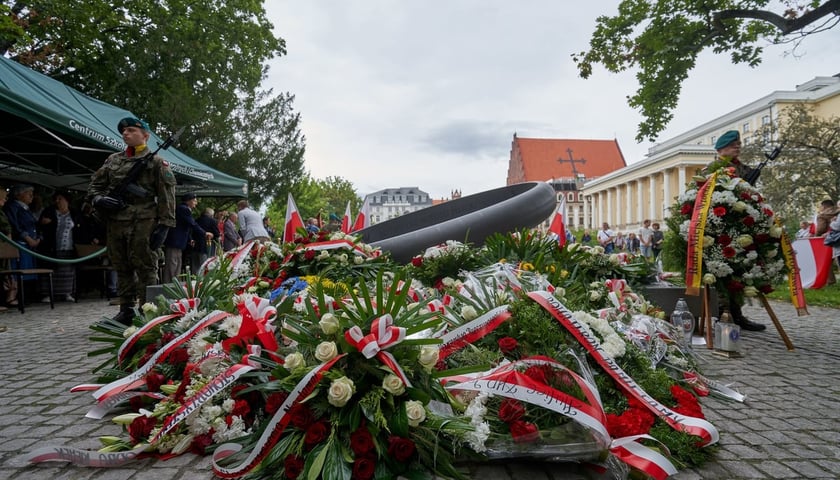 Uroczystość w rocznicę wybuchu Powstania Warszawskiego przy pomniku rotmistrza Witolda Pileckiego. Na zdjęciu wiązanki kwiatów złożone pod pomnikiem Witolda Pileckiego oraz dwóch żołnierzy pełniących wartę.