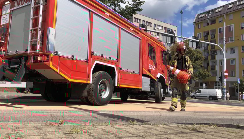 Na zdjęciu strażak przy wozie strażackim niesie pachołki drogowe do zabezpieczenia terenu
