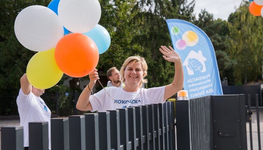 Dom opieki wytchnieniowej "KOKOSZKA" we Wrocławiu. Na zdjęciu uśmiechnięta kobieta z balonami w ręku, stojąca przy ogrodzeniu.