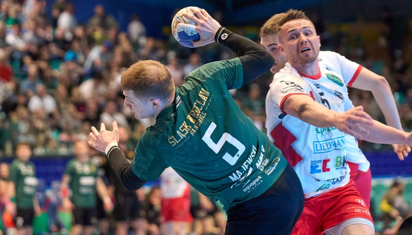 Kacper Majewski (zielony strój) w akcji rzutowej, za nim zawodnik MKS-u Wieluń w białej koszulce (hala Orbita, kwiecień 2024)
