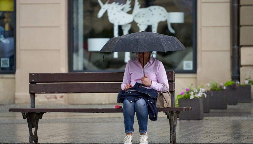 Deszcz we Wrocławiu. Na zdjęciu kobieta z parasolką siedząca na ławce. Zdjęcie archiwalne, ilustracyjne