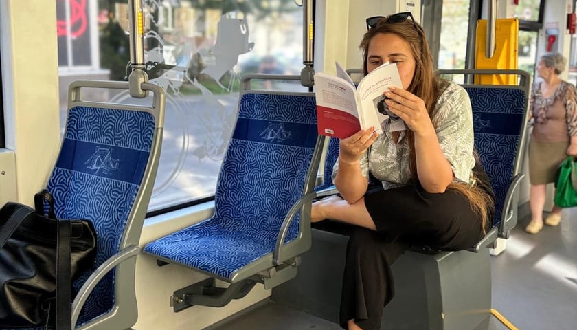 Na zdjęciu kobieta czytająca książkę w tramwaju.