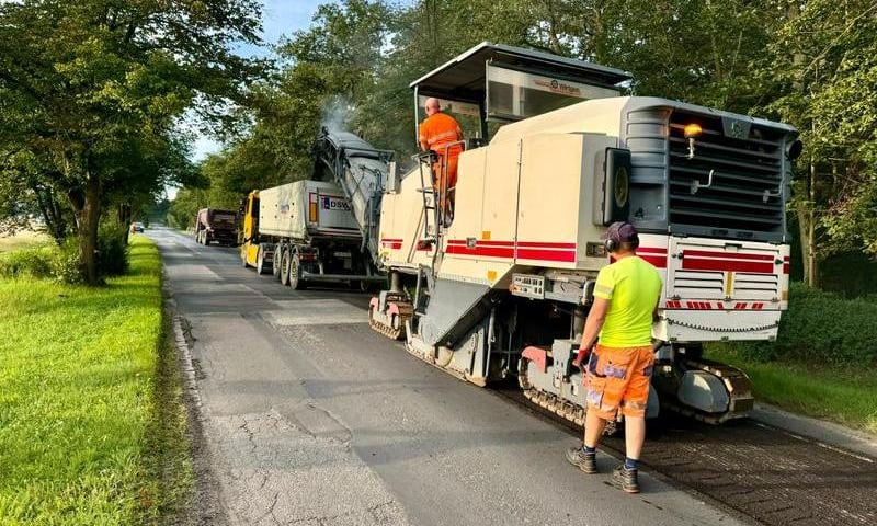 Mężczyzna w jaskrawym stroju przed jadącą maszyną budowlaną na ulicy Brodzkiej
