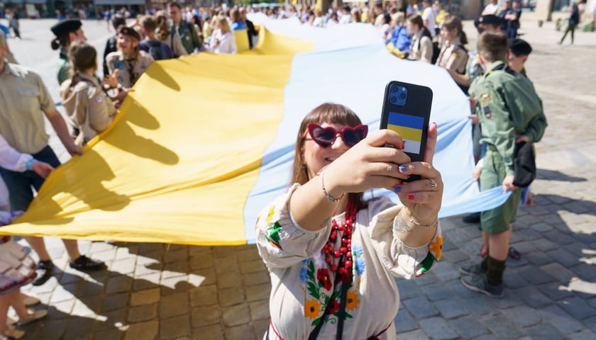 Kobieta robi zdjęcie telefonem z wielką flagą Ukrainy w tle