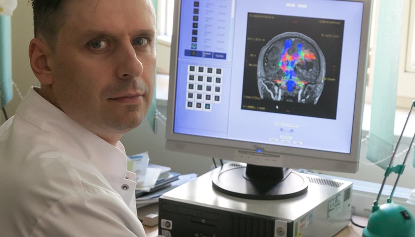 Prof. Paweł Tabakow, neurochirurg. Na zdjęciu mężczyzna siedzi przy biurku z komputerem