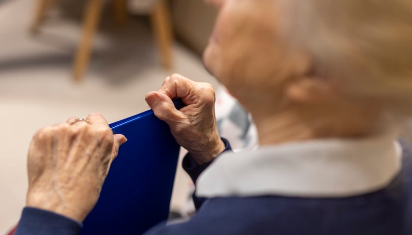 Seniorka trzymająca w dłoniach niebieską teczkę, zdjęcie ilustracyjne