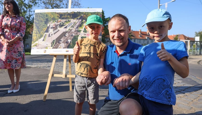 Radny osiedla Strachocin-Swojczyce-Wojnów z dwoma synami pozuje do zdjęcia na tle wizualizacji Trasy Autobusowo-Tramwajowej na Swojczyce