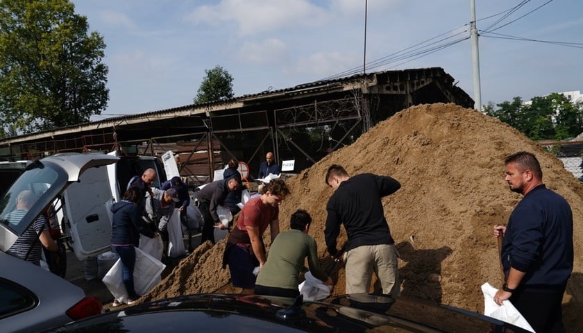 Kobiety i mężczyźni przesypujący piach do worków w punkcie na terenie ZDiUM-u przy ul. Długiej