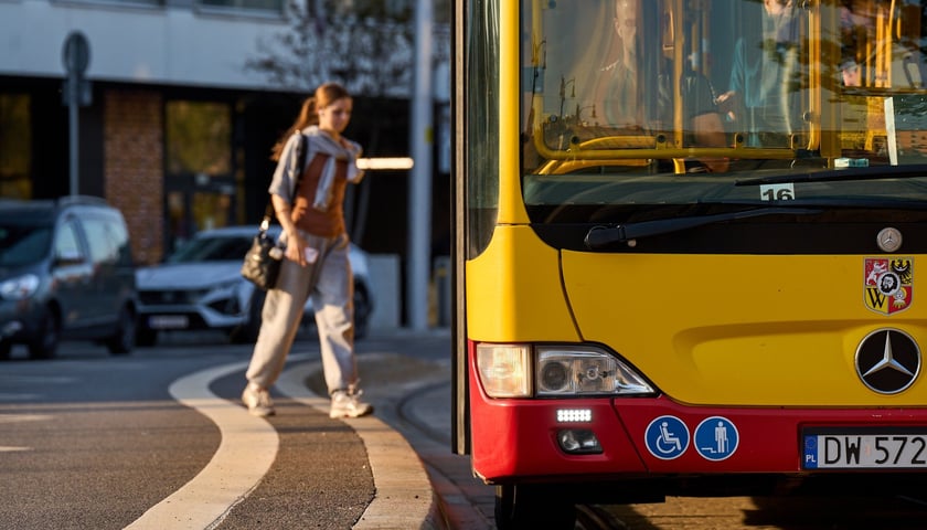 Fragment miejskiego autobusu, na drugim planie pasażerka 
