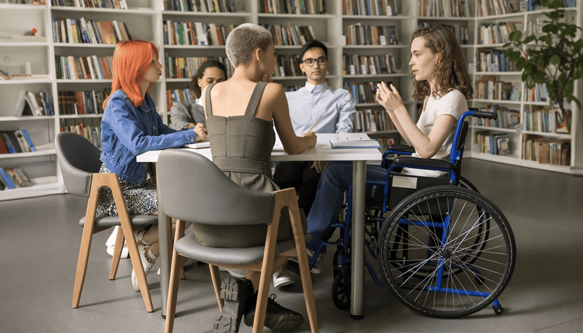 Młoda kobieta na wózku inwalidzkim siedząc przy stole z innymi studentami 