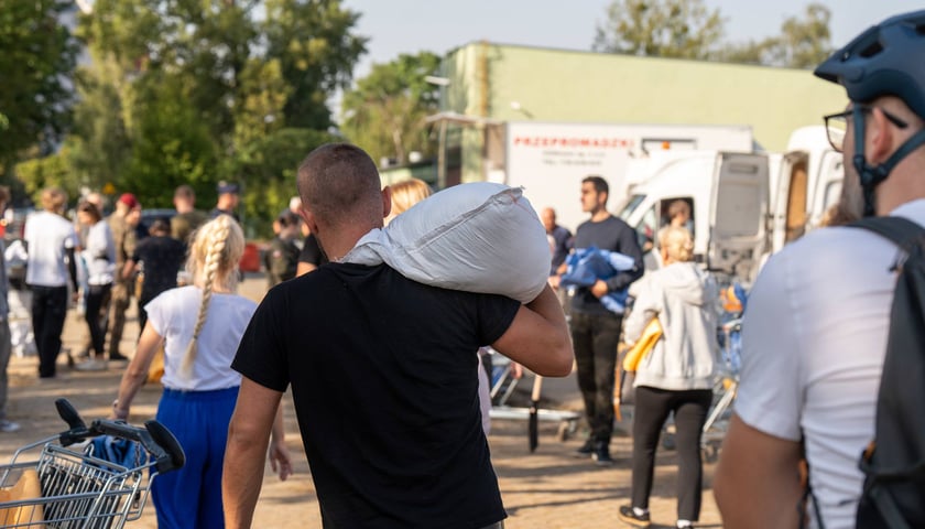 Mężczyzna ubrany w czarną koszulę niesie na barku worek z piachem