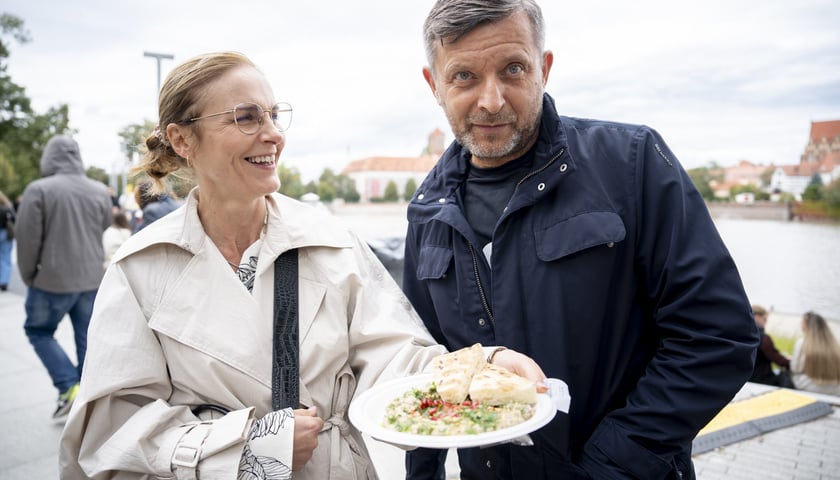 Finał Gastro Miasto na bulwarze Dunikowskiego - 28 września. Od lewej: uśmiechnięta kobieta w jasnym płaszczu pokazuje talerz z potrawą, obok mężczyzna w ciemnej kurtce.