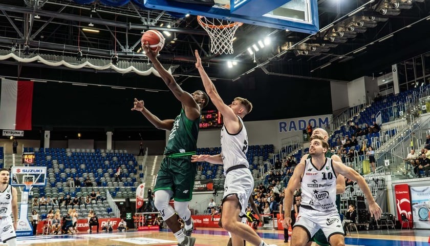 Isaiah Whitehead (zielony strój) w wyskoku z piłką pod koszem, przy nim zawodnik Legii Warszawa (biały strój)