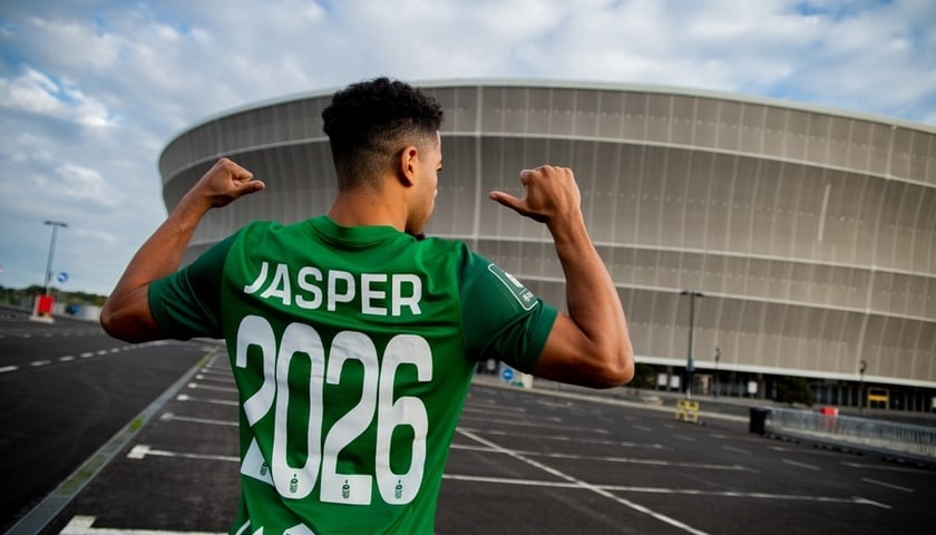 Sylvester Jasper stoi obrócony plecami (w koszulce zielonej z numerem 2026) na tle stadionu miejskiego