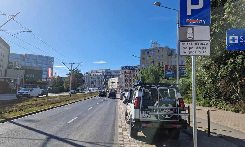 Znak drogowy P, zaparkowane samochody, ulica i budynki 