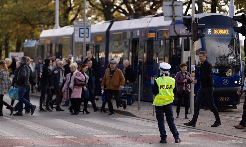 Policjantka tyłem do aparatu fotograficznego czuwa nad ruchem ludzi wysiadającyh z tramwaju linii specjalnej pod Cmentarzem Osobowickim - zdjęcie z dnia Wszystkich Świętych z ubiegłego roku