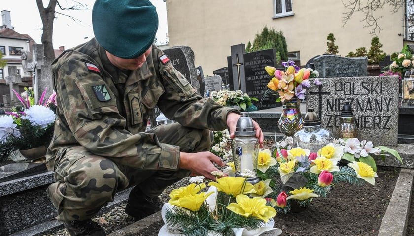 Żołnierz w mundurze polowym  układa kwiaty na grobie