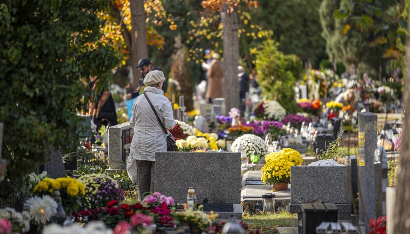 Kobieta w jasnej kurtce i berecie, stojąca wśród grobów na cmentarzu przy ul. Smętnej