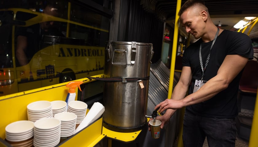 Mężczyzna w środku autobusu Streetbus nalewa gorącą wodę z termosu do kubka